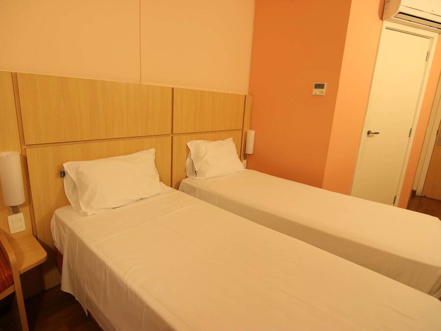 Una habitación de hotel con dos camas individuales, cabecero de madera, unidad de aire acondicionado y una puerta.