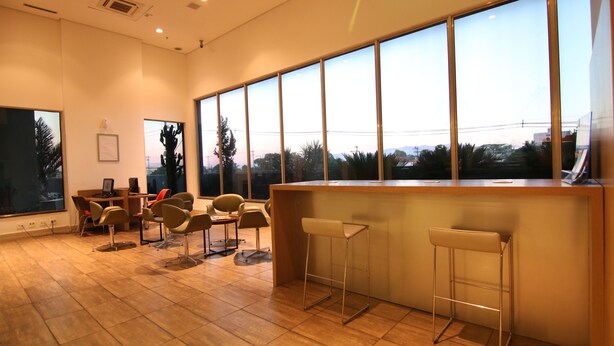 A modern bar area with a wooden counter, bar stools, and large windows offering a view of the cityscape. - Samba Itaboraí (Itaborai)