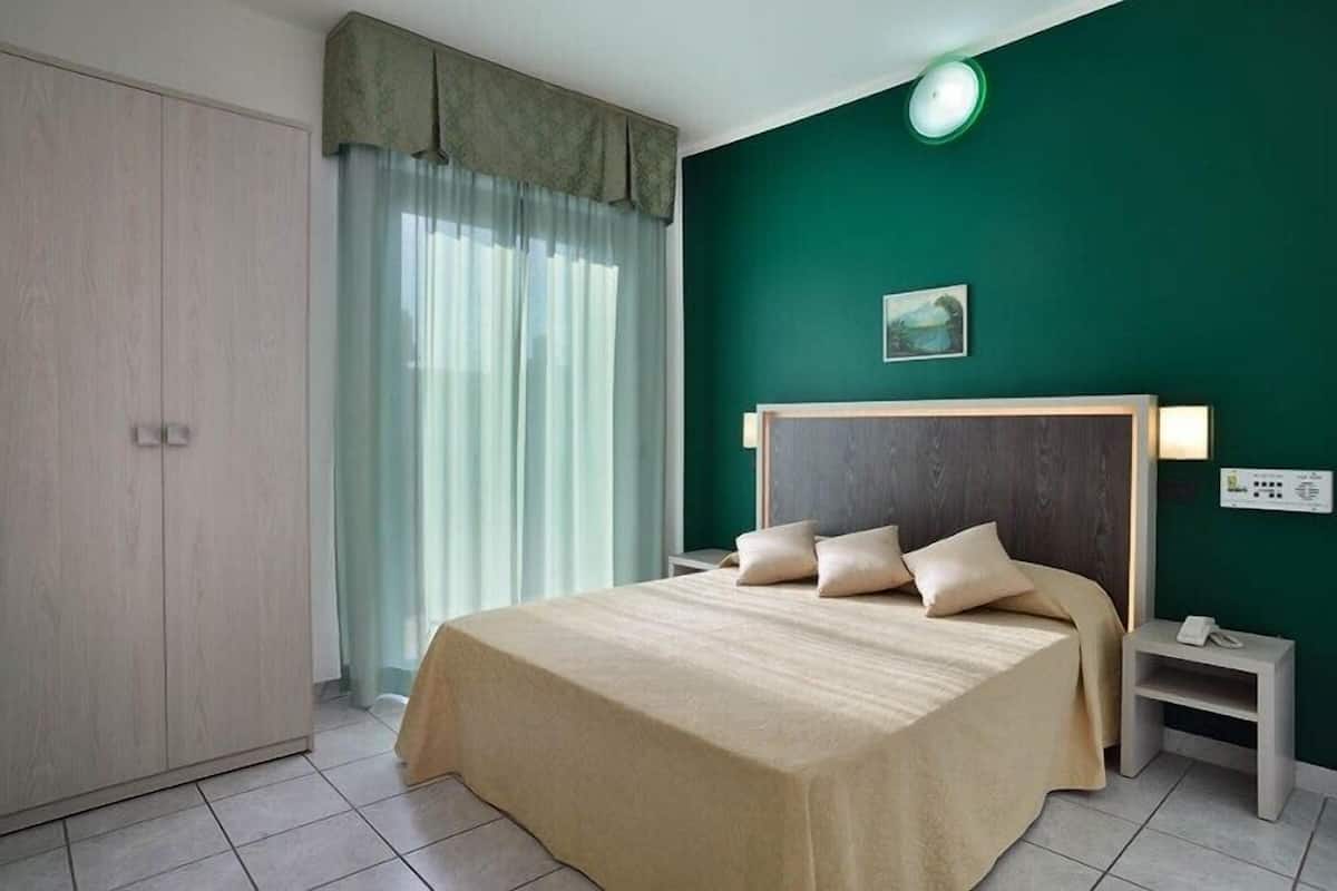 A hotel room with a bed, nightstand, and a green wall.