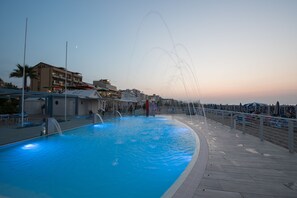 A swimming pool with a water fountain feature, a boardwalk, and a view of the sunset. - Residence Margherita (Cattolica)