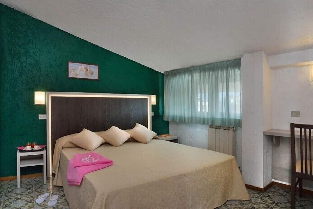 A hotel room with a large bed, a small bedside table, a chair, and a window with curtains.