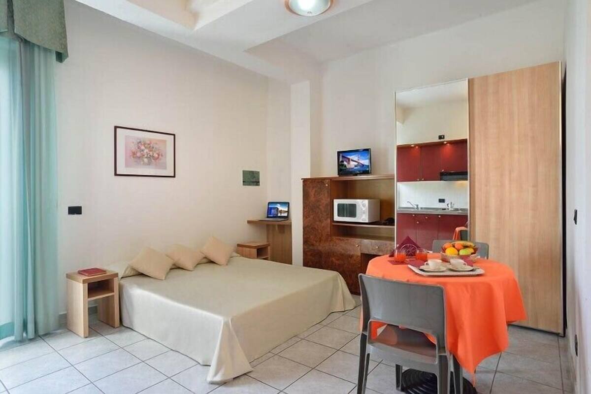 A hotel room with a bed, bedside table, TV, microwave, and a small dining area with a table and chairs.