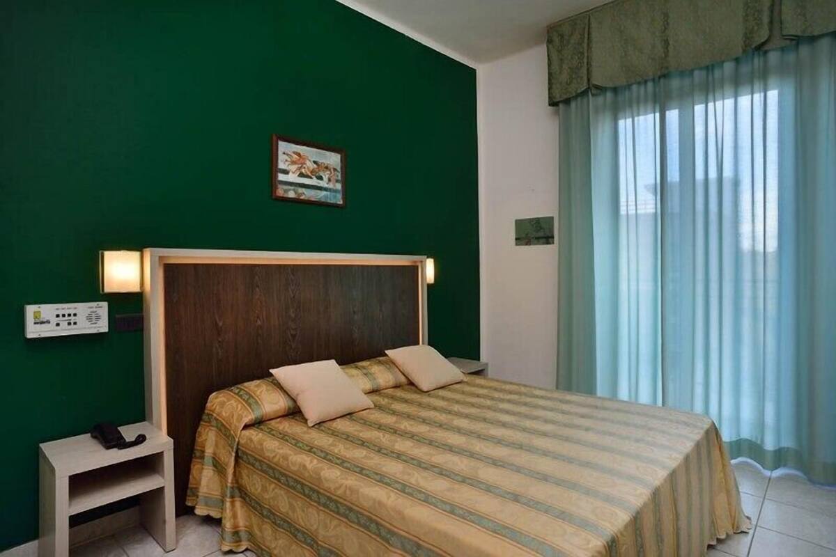 A hotel room with a bed, bedside table, and a wall-mounted control panel.