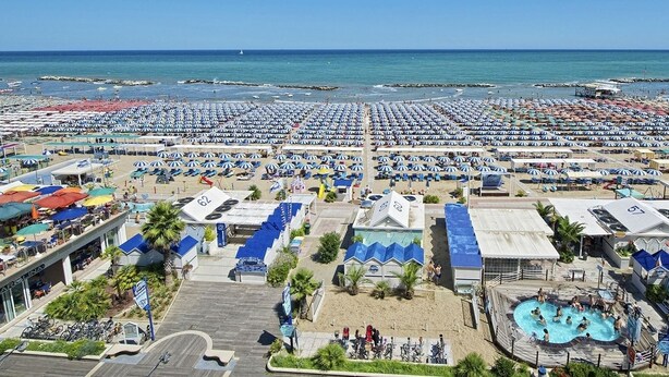 Un resort frente al mar con numerosas sombrillas, una piscina y servicios en la playa.