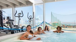 Zona de piscina interior con equipo de ejercicios y vista a la playa.