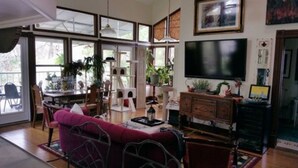 Ein geräumiges Wohnzimmer mit großem Fernseher, einer Couch und einem Essbereich mit Stühlen und einem Tisch.