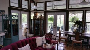 Ein geräumiges Zimmer mit großem Fenster, einem Essbereich und einer gemütlichen Sitzecke mit rotem Sofa und einer Katze.