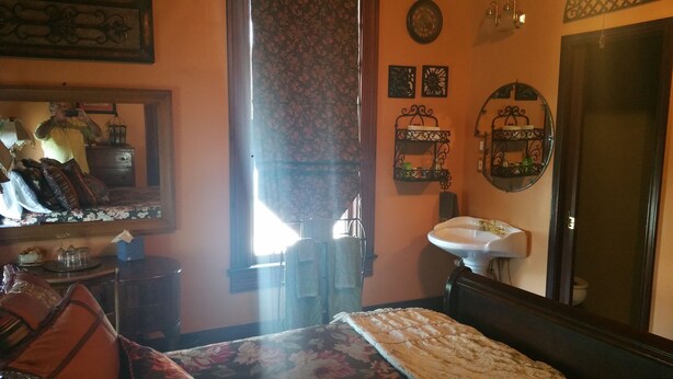A bedroom with a bed, a dresser, a mirror, a sink, and a door. - Fig Tree Manor (Palestine)
