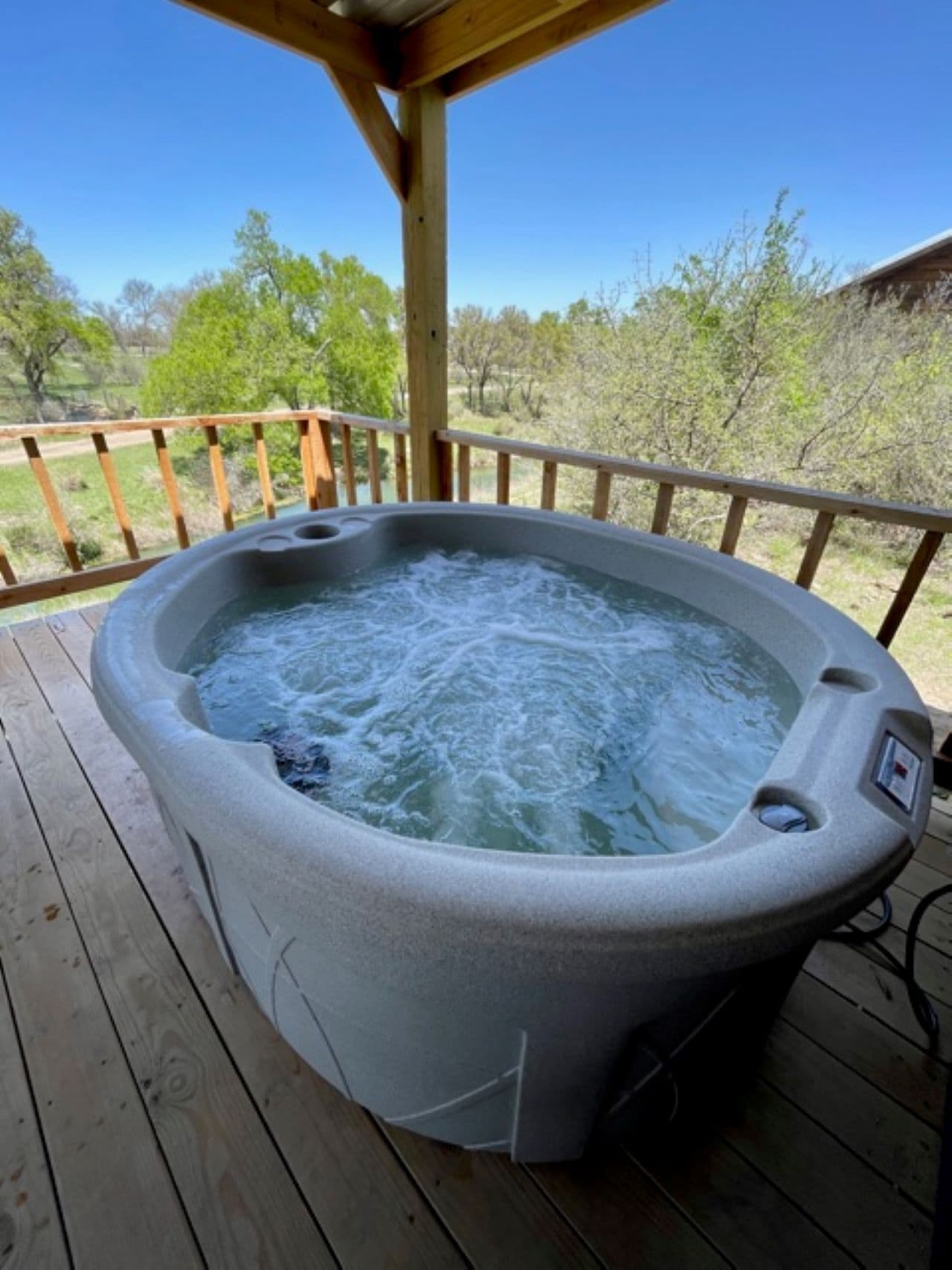 A hot tub on a wooden deck with a clear view of trees and a building in the background.