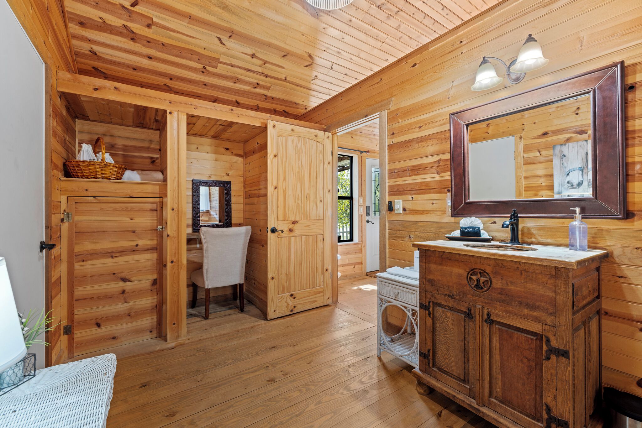 Ein Holzblockhaus-Innenraum mit einer Holztür, einem Waschbecken mit Spiegel und einem Korb auf einem Regal.