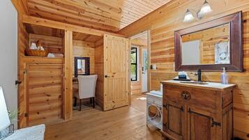 A wooden cabin interior with a wooden door, a sink with a mirror, and a basket on a shelf.