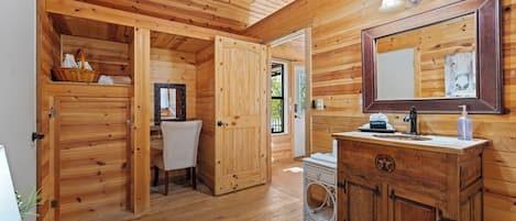 Ein Holzblockhaus-Innenraum mit einer Holztür, einem Waschbecken mit Spiegel und einem Korb auf einem Regal.
