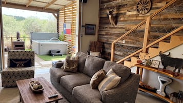 A cozy living room with a sofa, coffee table, and decorative pillows. A wooden staircase with a wall-mounted animal head decoration is visible.