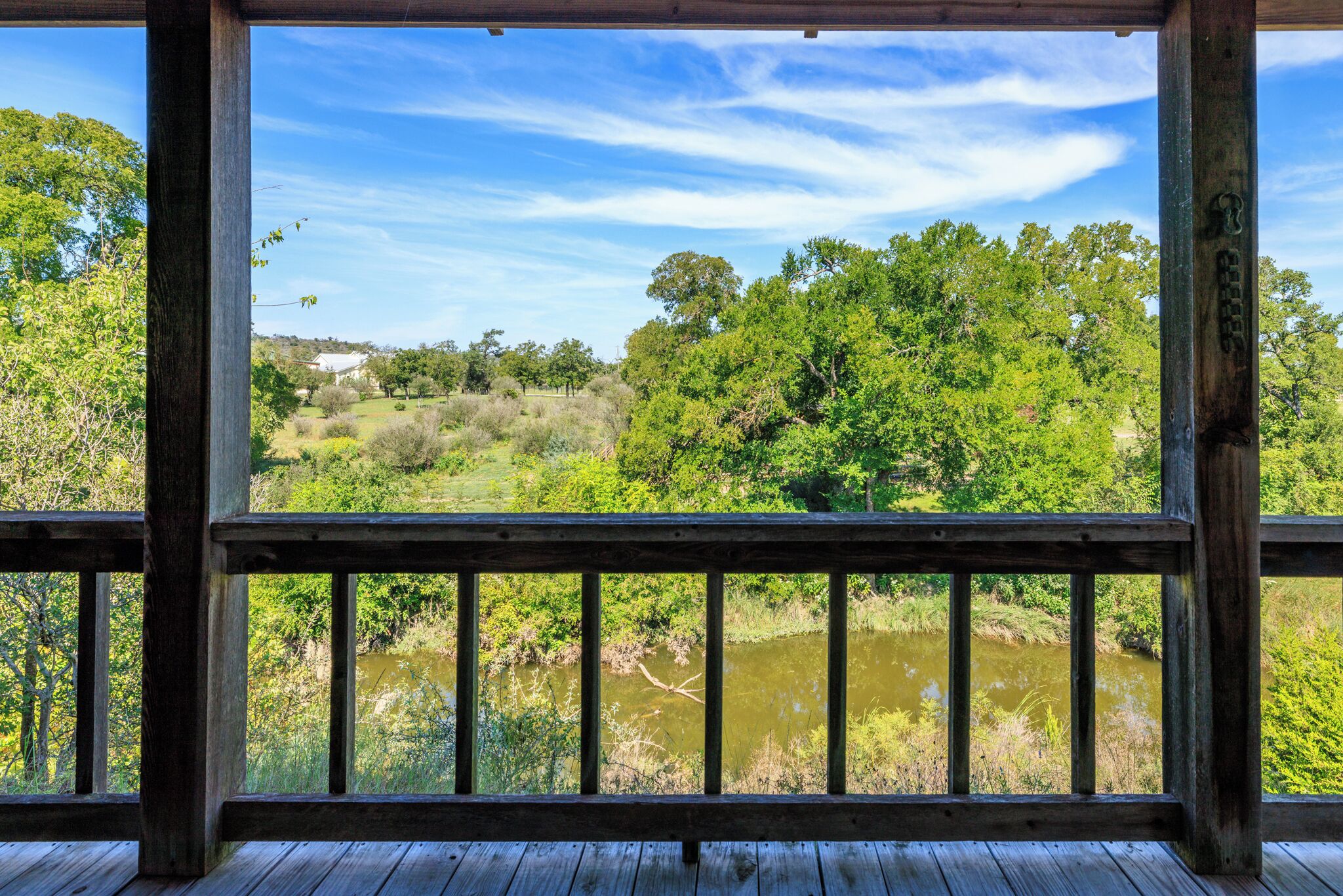 A wooden deck with a view of a river and surrounding greenery.