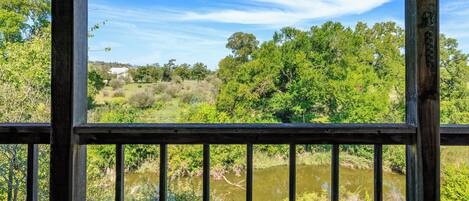 A wooden deck with a view of a river and surrounding greenery.