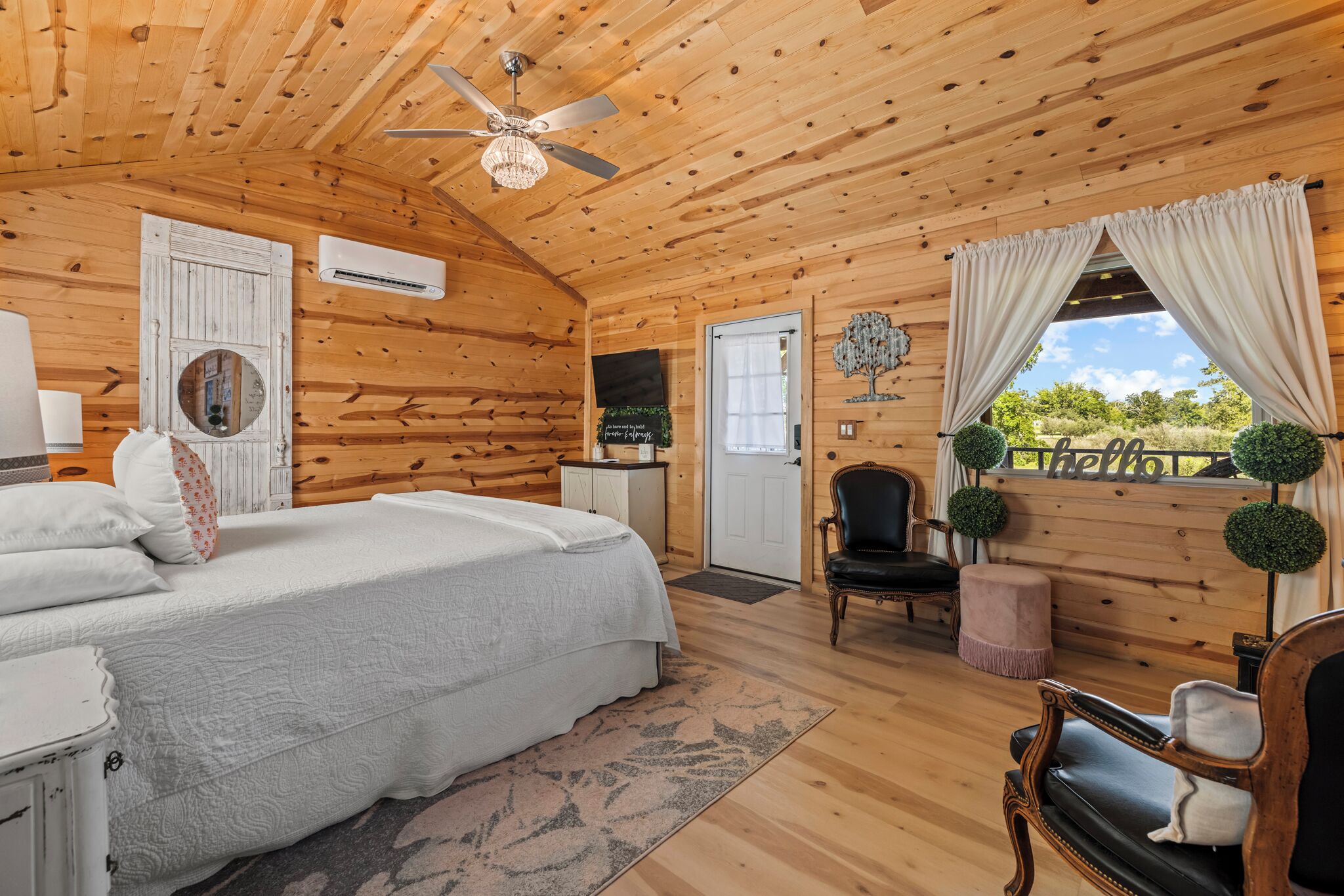 Ein Schlafzimmer einer Holzhütte mit einem Bett, einem Sessel, einem kleinen Tisch und einem Deckenventilator.