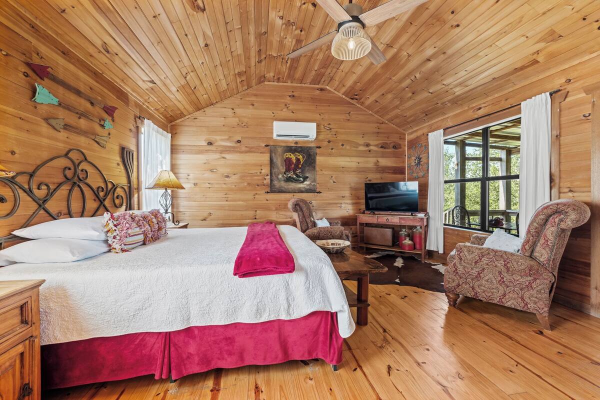Een houten slaapkamer met een bed, een stoel, een televisie en een raam.