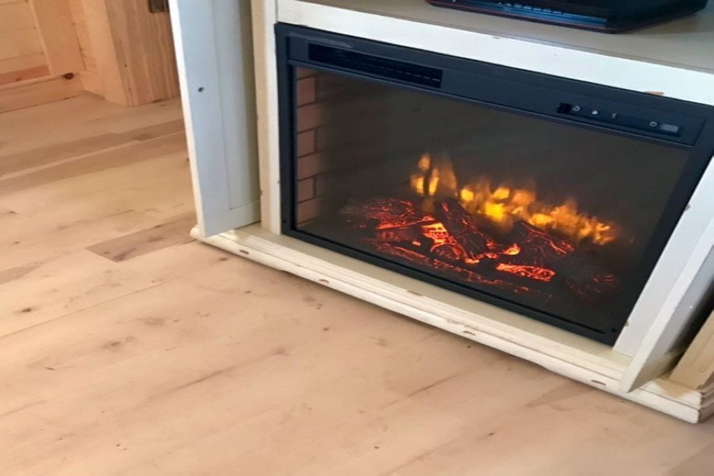A fireplace with visible flames, a white frame, and a wooden floor.