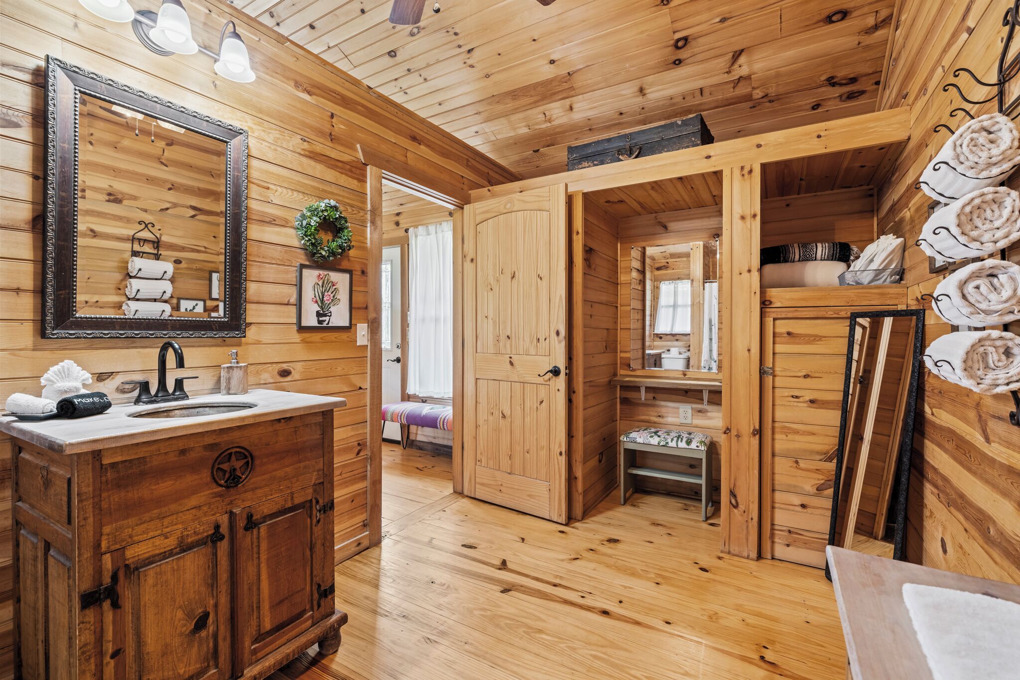 A wooden cabin interior with a wooden vanity, a mirror, a sink, and a door leading to a sleeping area.