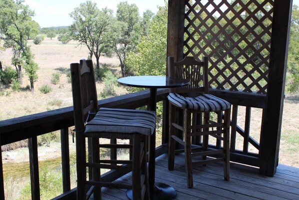 A wooden deck with a table and two chairs, overlooking a natural landscape with trees and a field. - City on a Hill at Spring Creek (Fredericksburg)