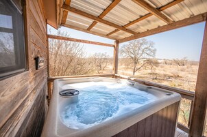 Een houten hut met een hottub en uitzicht op een droog landschap.
