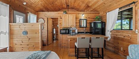Interior acogedor de una cabaña con techo de madera, una kitchenette, zona de comedor y una cama.