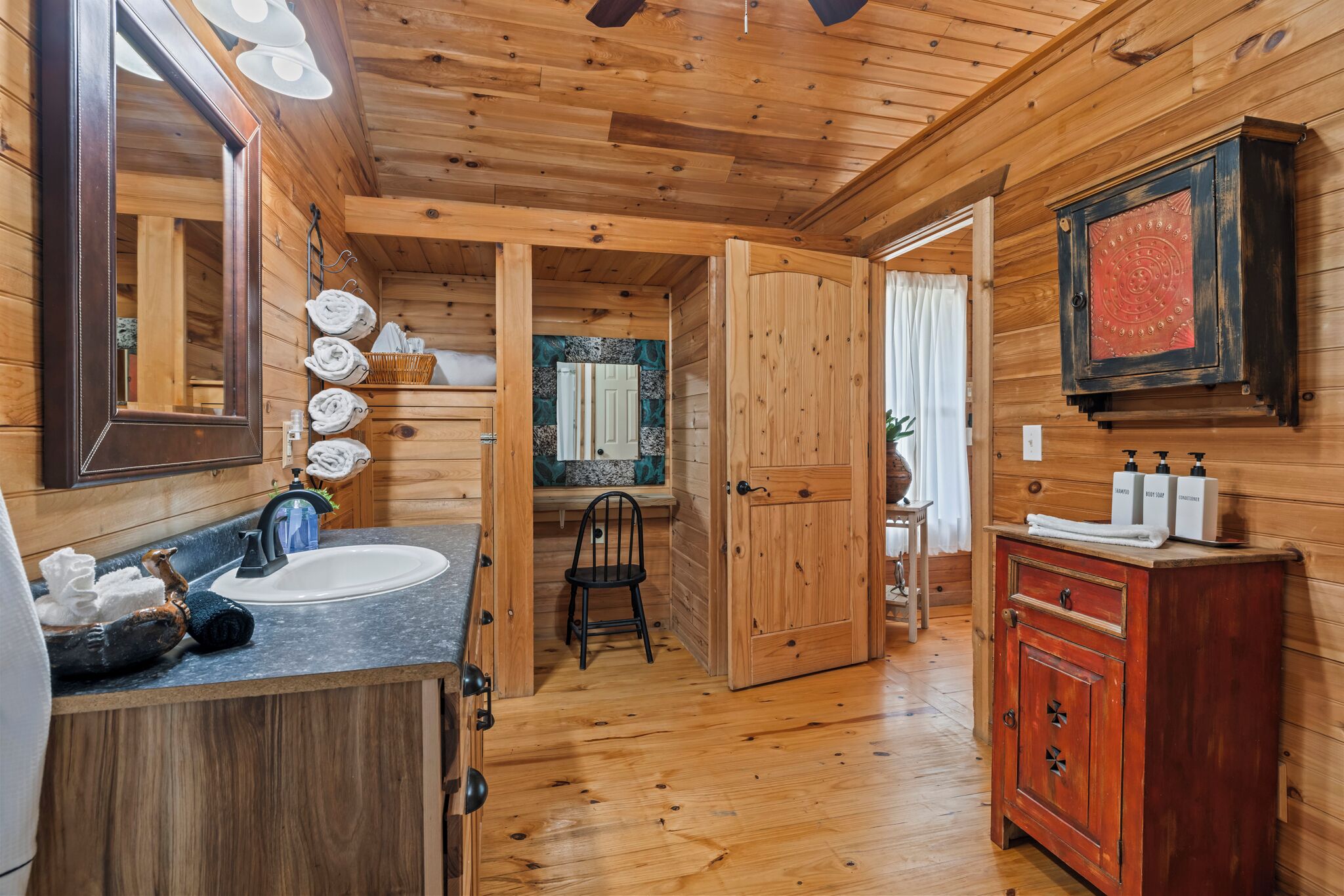 Une salle de bain rustique, avec une cabine en bois, un lavabo, un miroir et des armoires en bois.