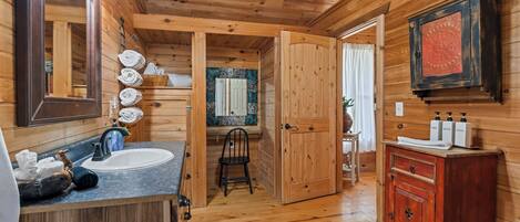 Une salle de bain rustique, avec une cabine en bois, un lavabo, un miroir et des armoires en bois.