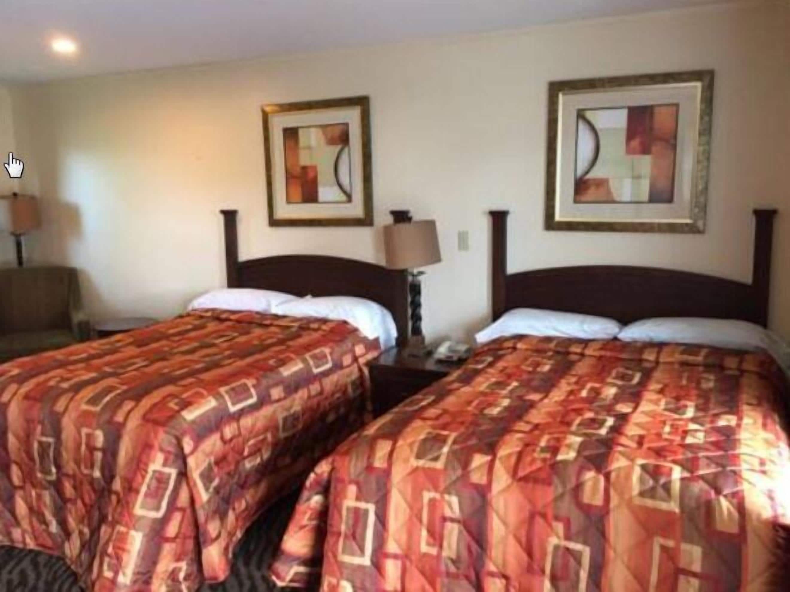 A hotel room with two beds, each with a patterned bedspread, a nightstand with a lamp, and framed artwork on the wall.