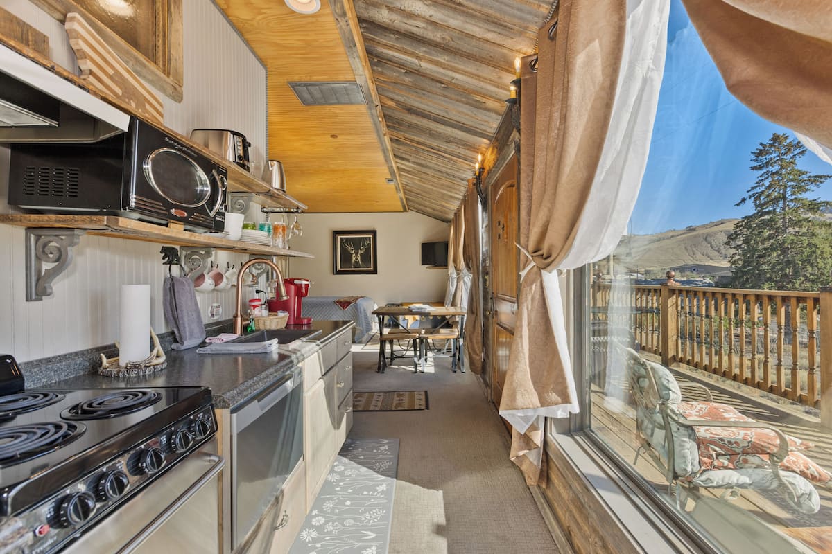 A compact kitchen with a stove, microwave, and various kitchen items. There is a dining area with a table and chairs, and a window with a view of the outdoors.
