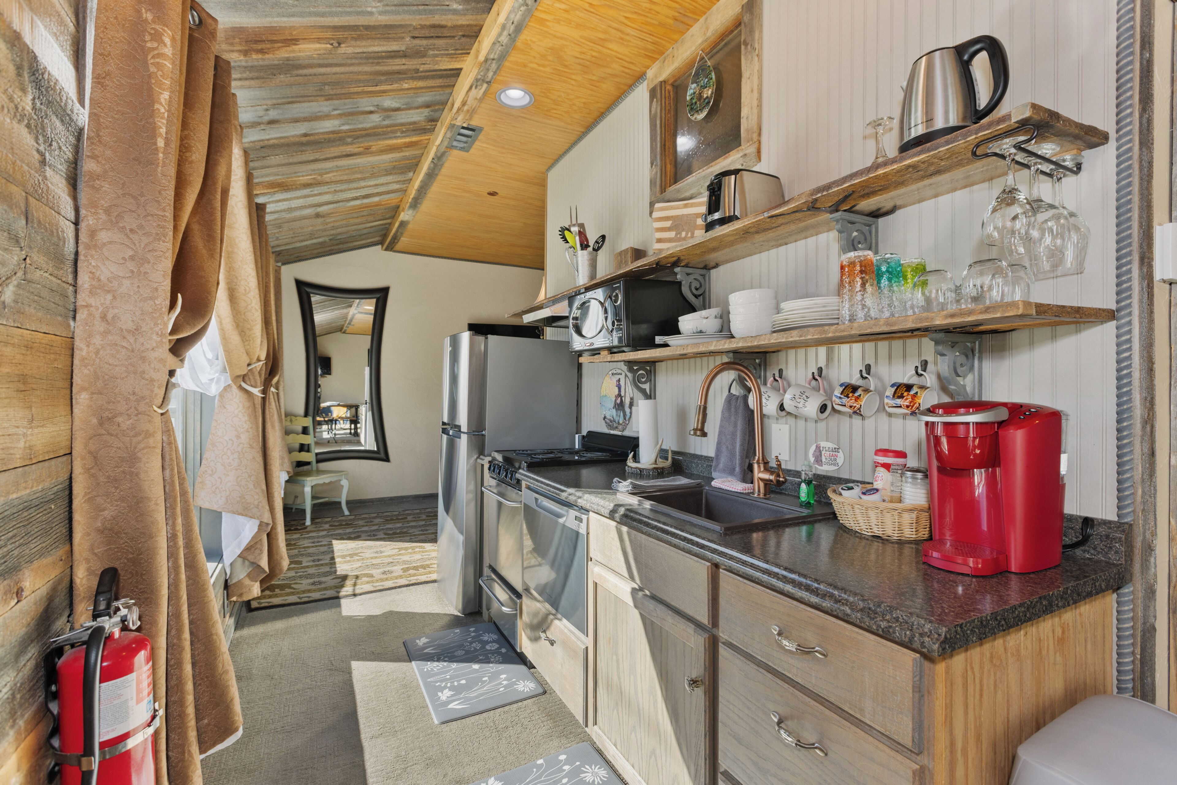 Eine kleine Küche mit Holzausbau, einem Edelstahlkühlschrank, einer Kaffeemaschine und verschiedenen Küchenutensilien auf der Arbeitsplatte.