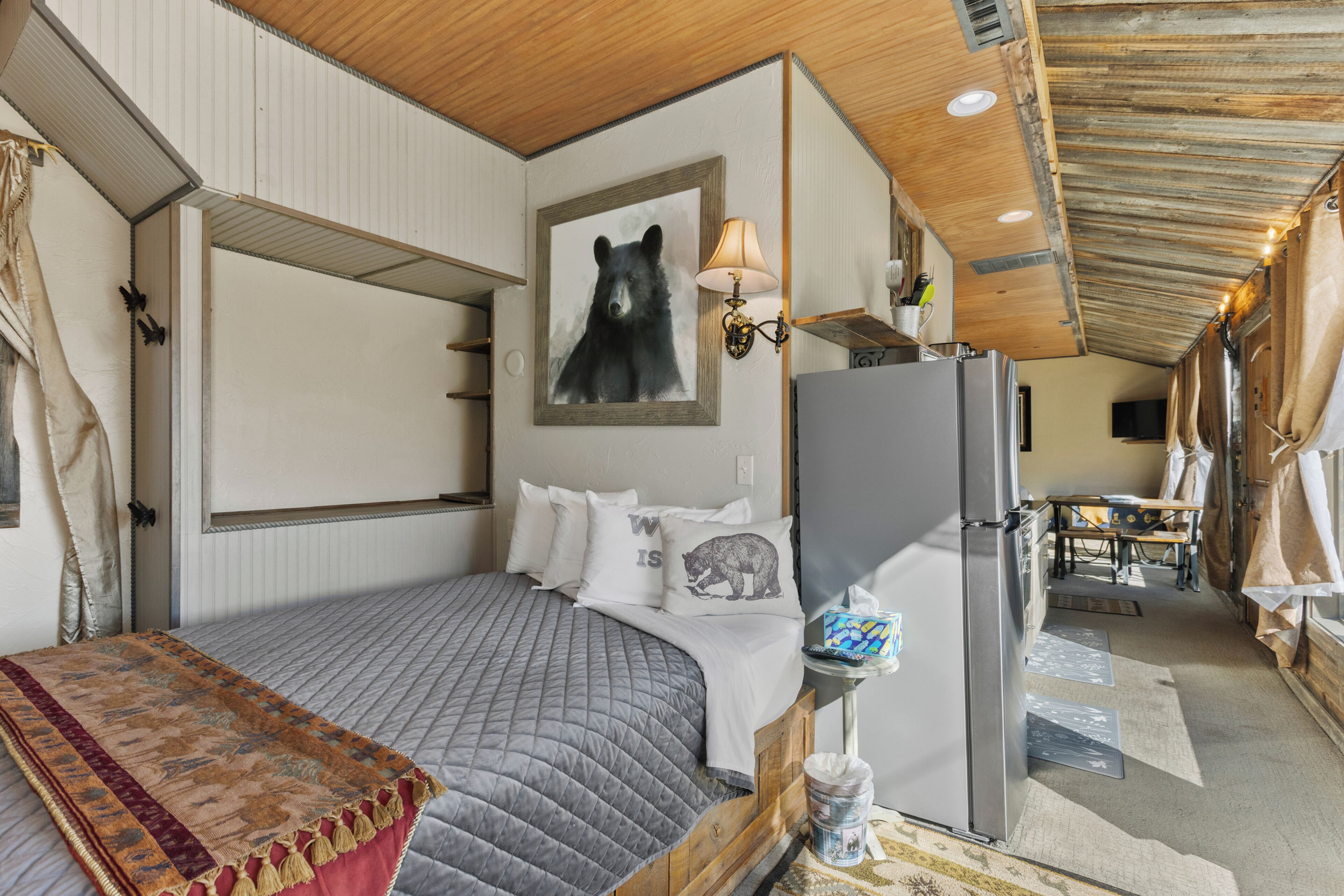 A cozy bedroom with a bed, a refrigerator, a lamp, and a bear-themed pillow.