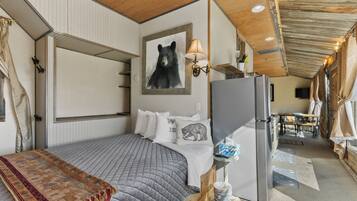 A cozy bedroom with a bed, a refrigerator, a lamp, and a bear-themed pillow.