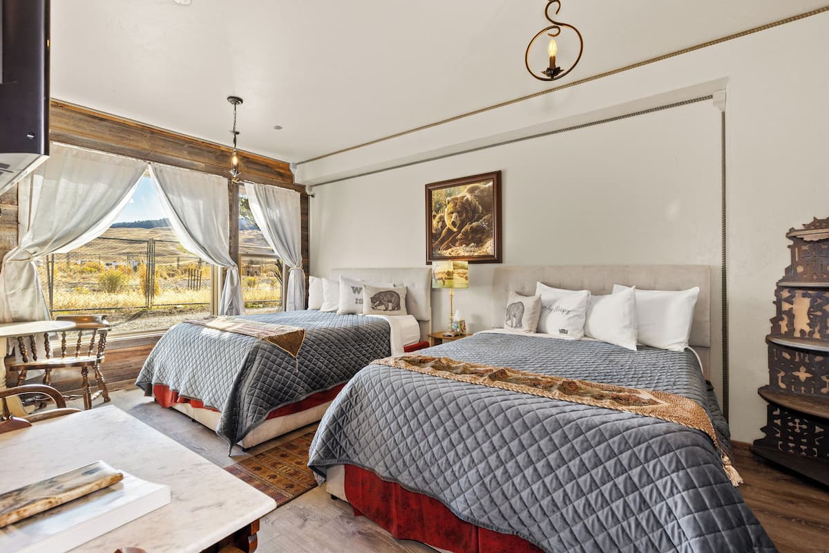 A bedroom with two beds, a wooden table, and a view of the outdoors.