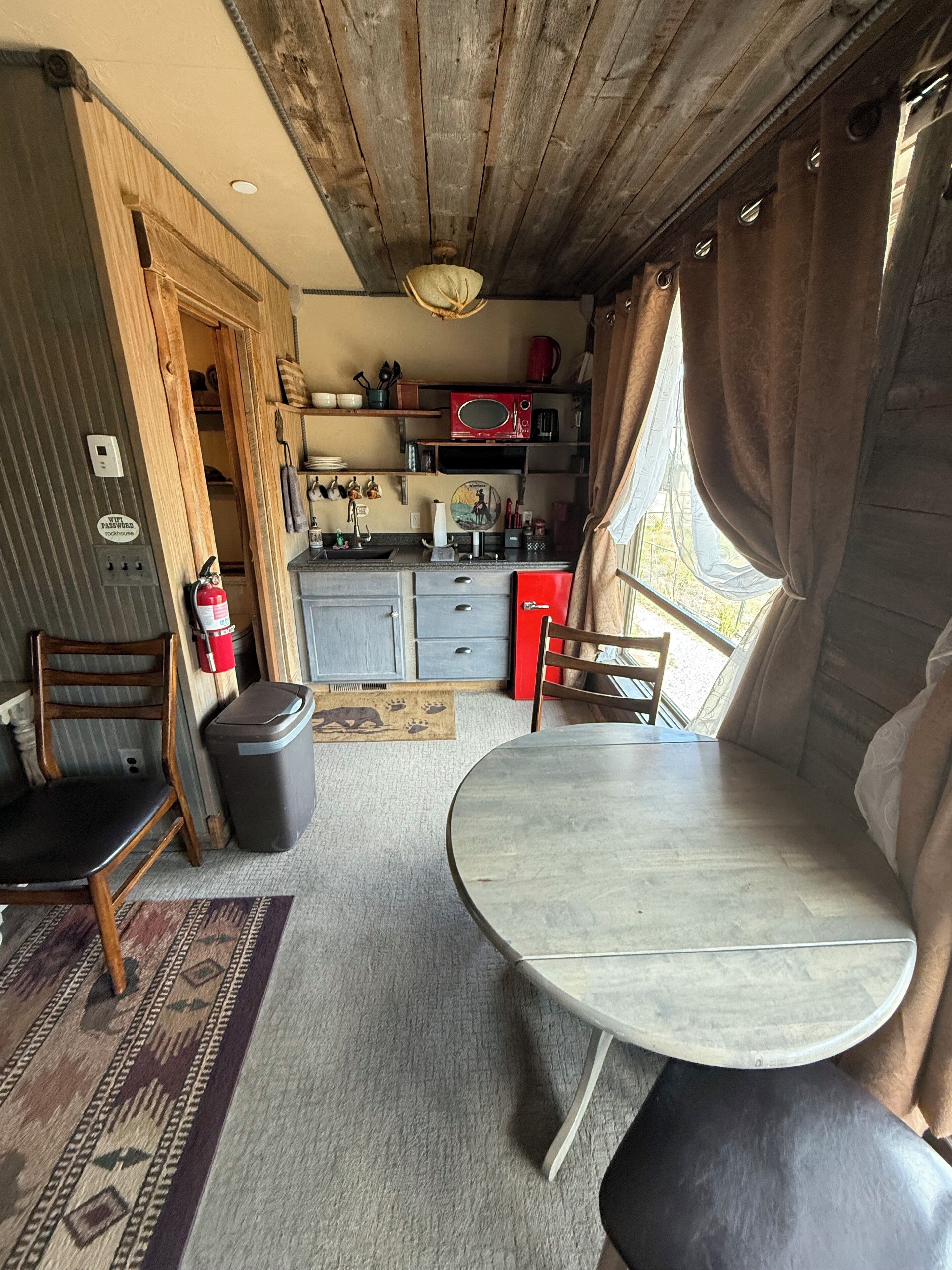 Une cuisine compacte équipée d’un four à micro-ondes, d’un évier et de placards. On y trouve une table à manger avec des chaises et un tapis.