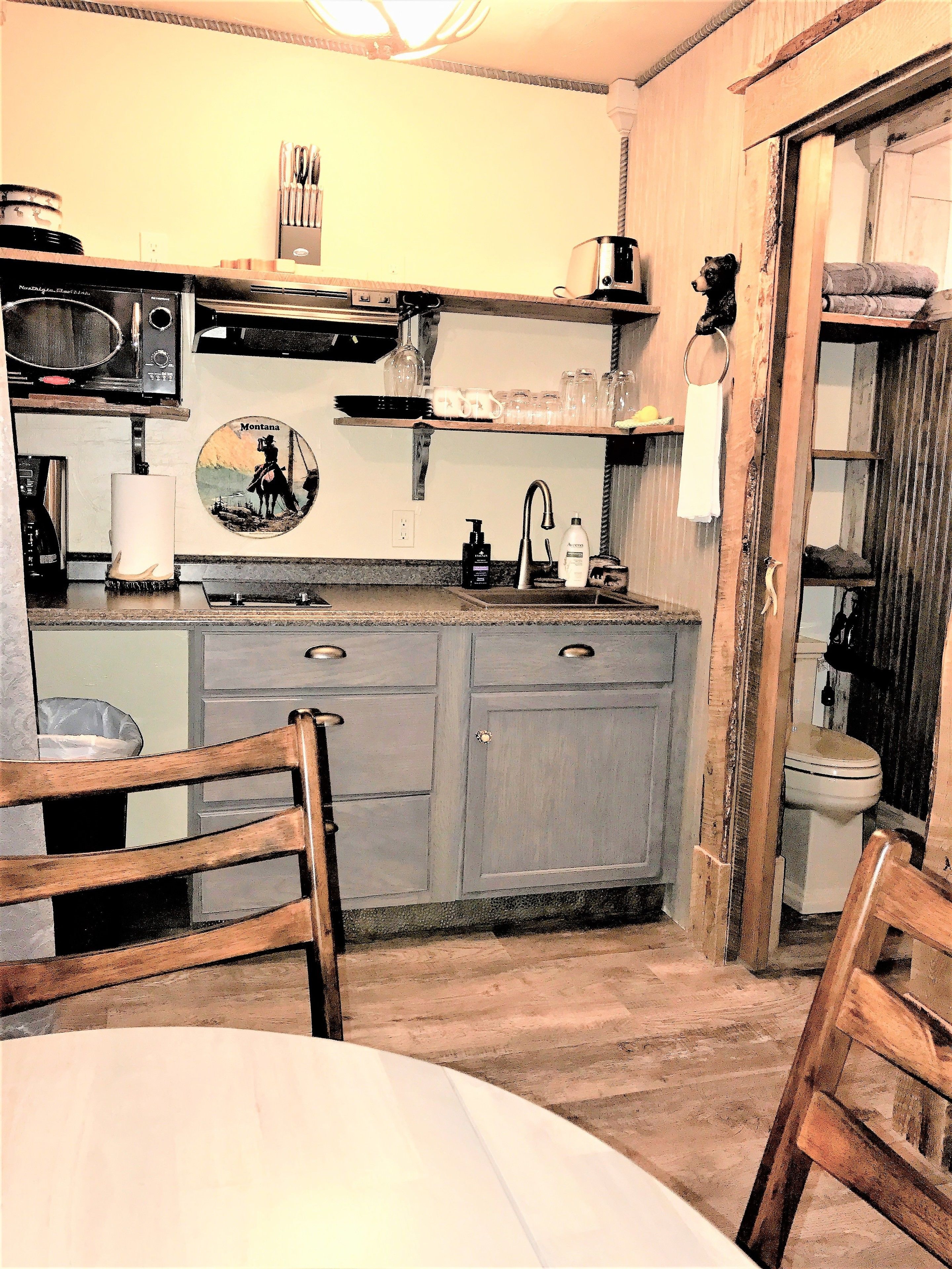 A rustic kitchen with wooden cabinets, a sink, and a dining area with chairs.