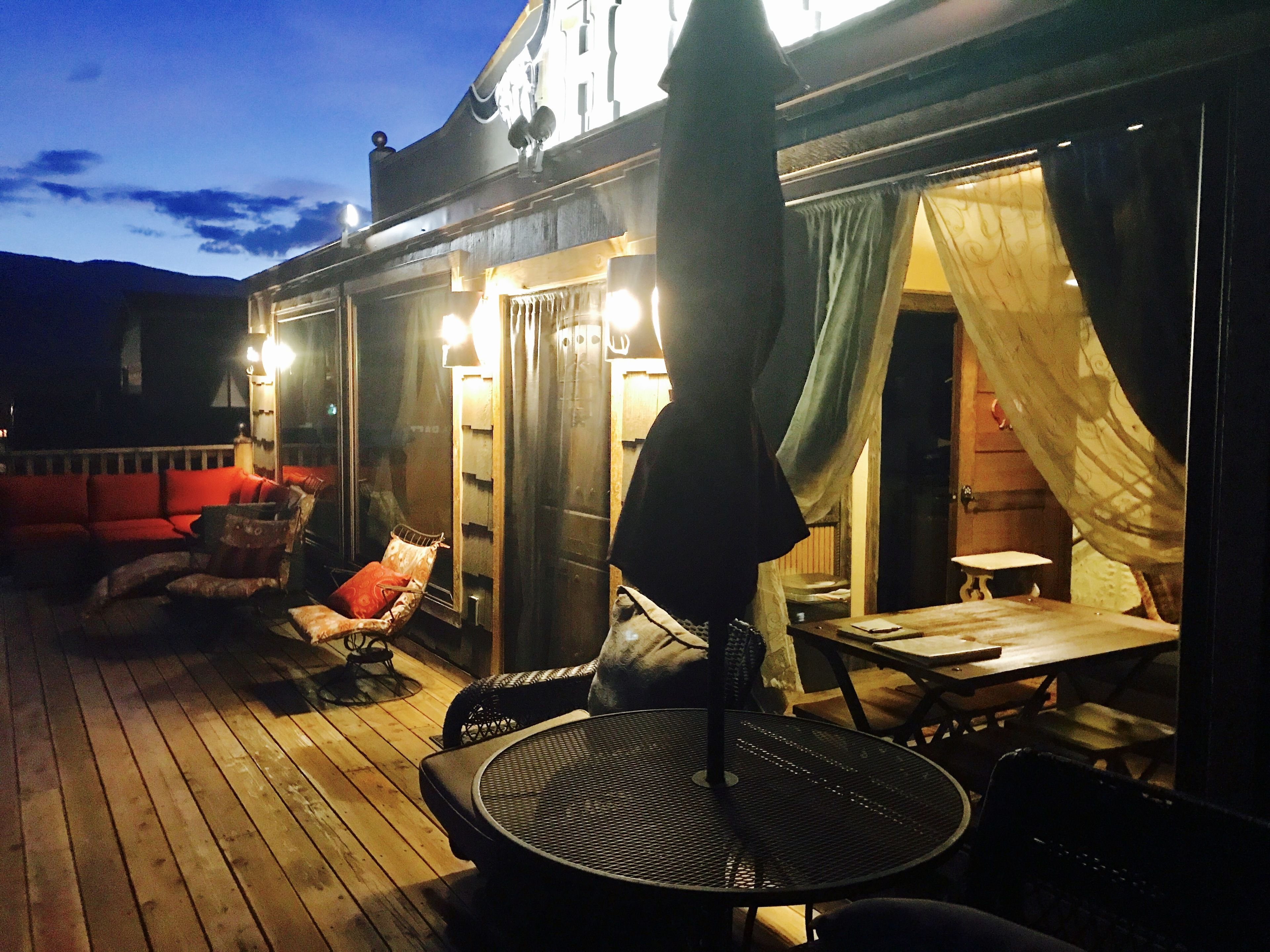 Et udendørs opholdsområde med træterrasse, et rundt metalbord og en rød sofa.