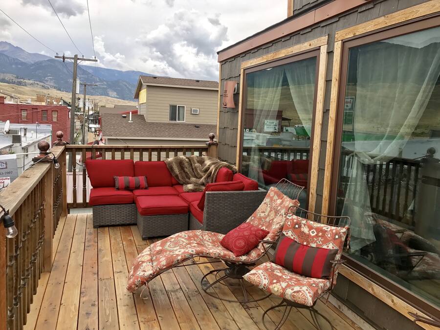 Ein Balkon mit einer roten Couch, gemusterten Stühlen und Blick auf Berge.