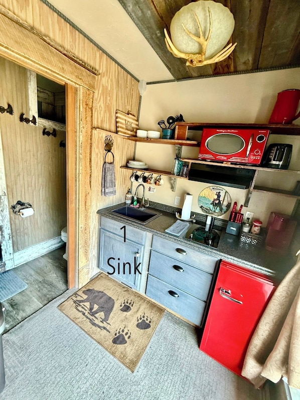 A compact kitchen with a single sink, wooden cabinets, and a red refrigerator.