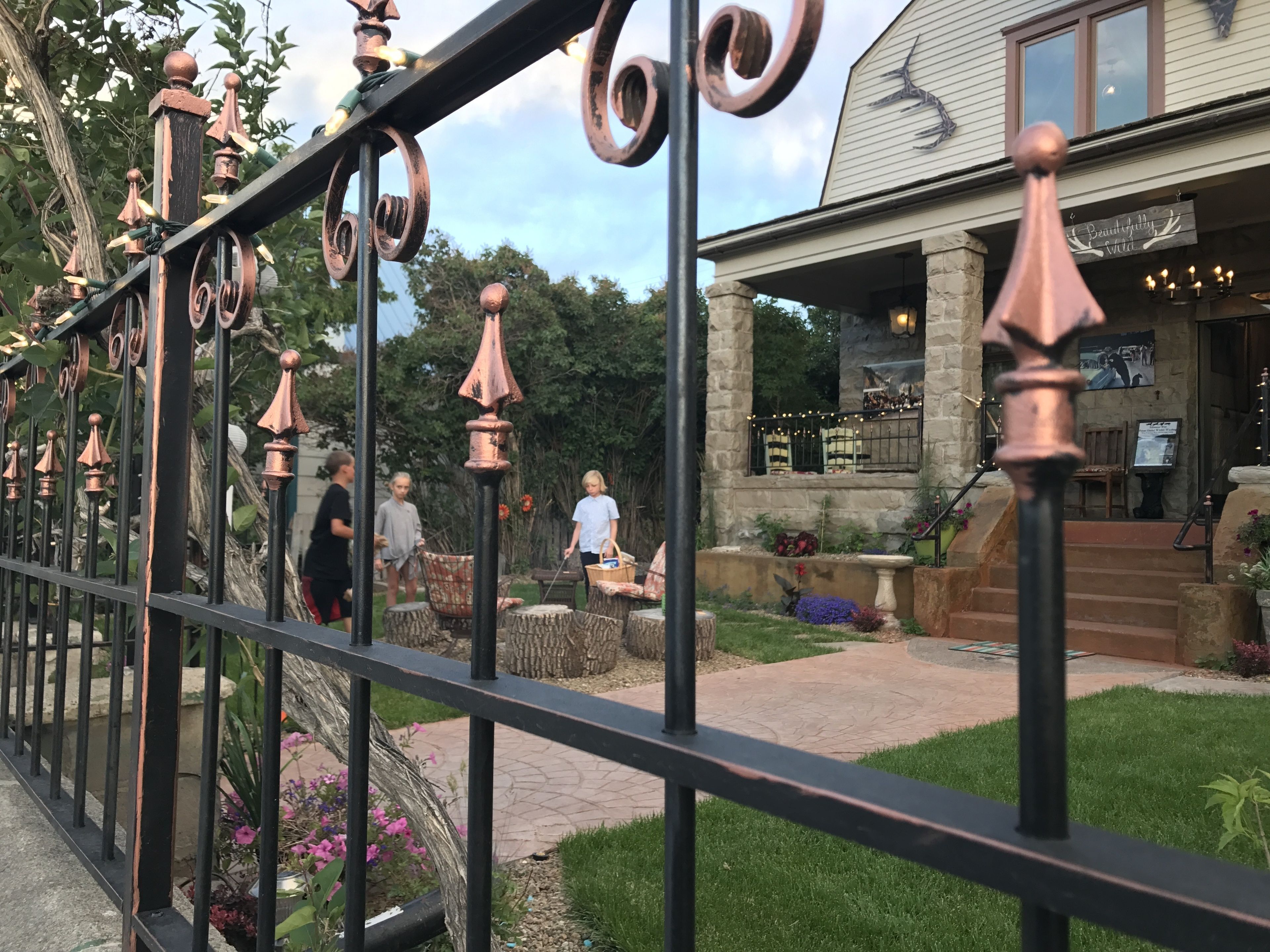 A wrought iron fence with decorative elements, a stone building with a sign, and a pathway leading to a seating area.