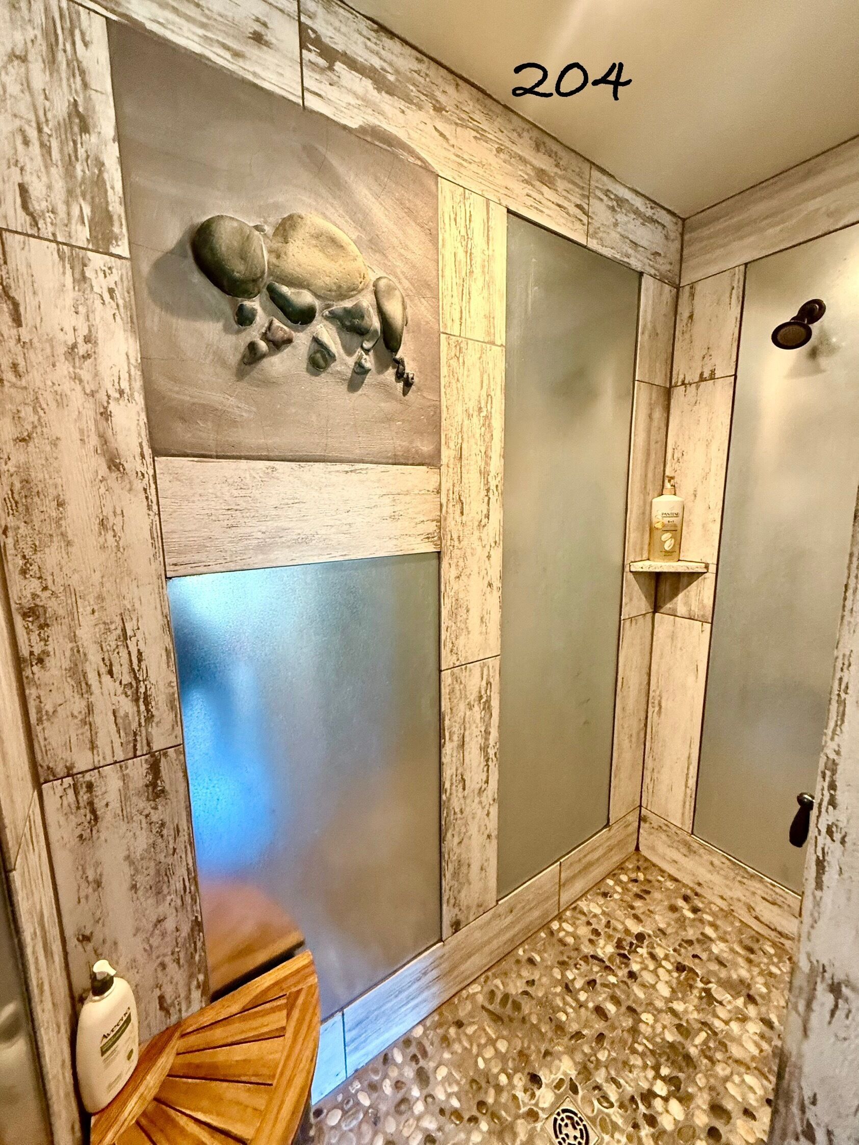 A bathroom with a rustic design, featuring a shower area with a textured wall and a patterned floor.