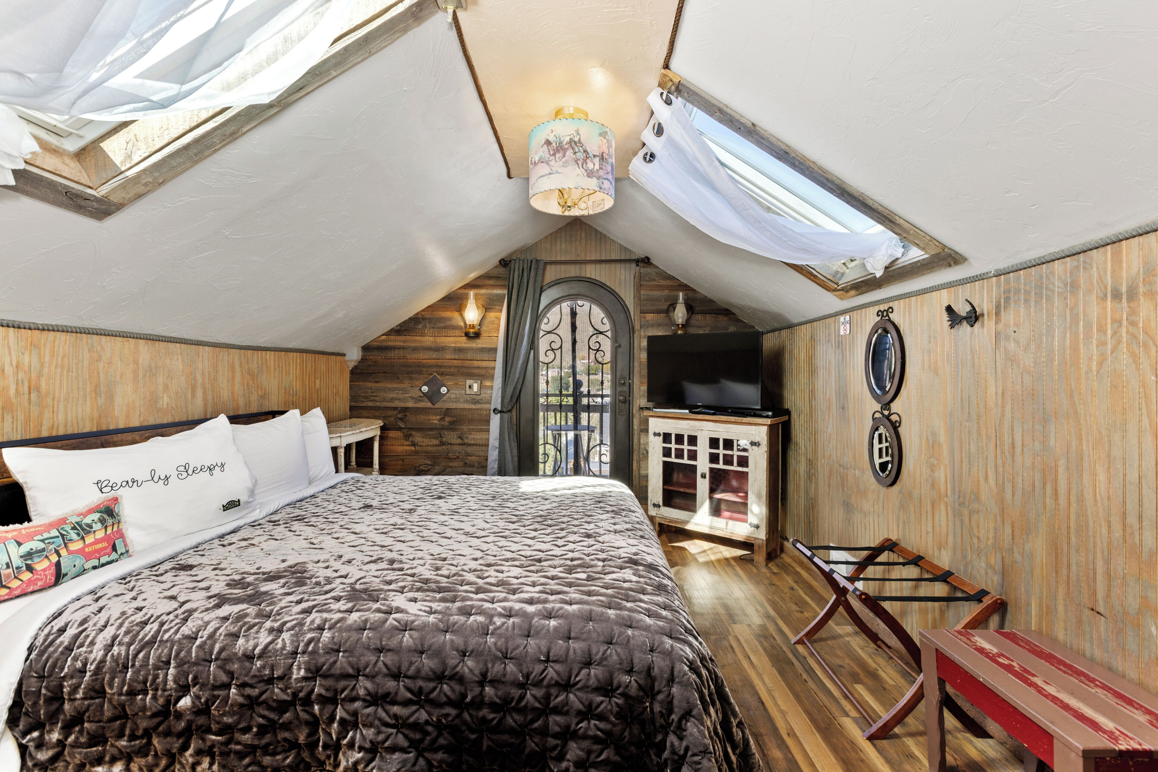 A bedroom with a large bed, wooden walls, a skylight, a television, and a small table.