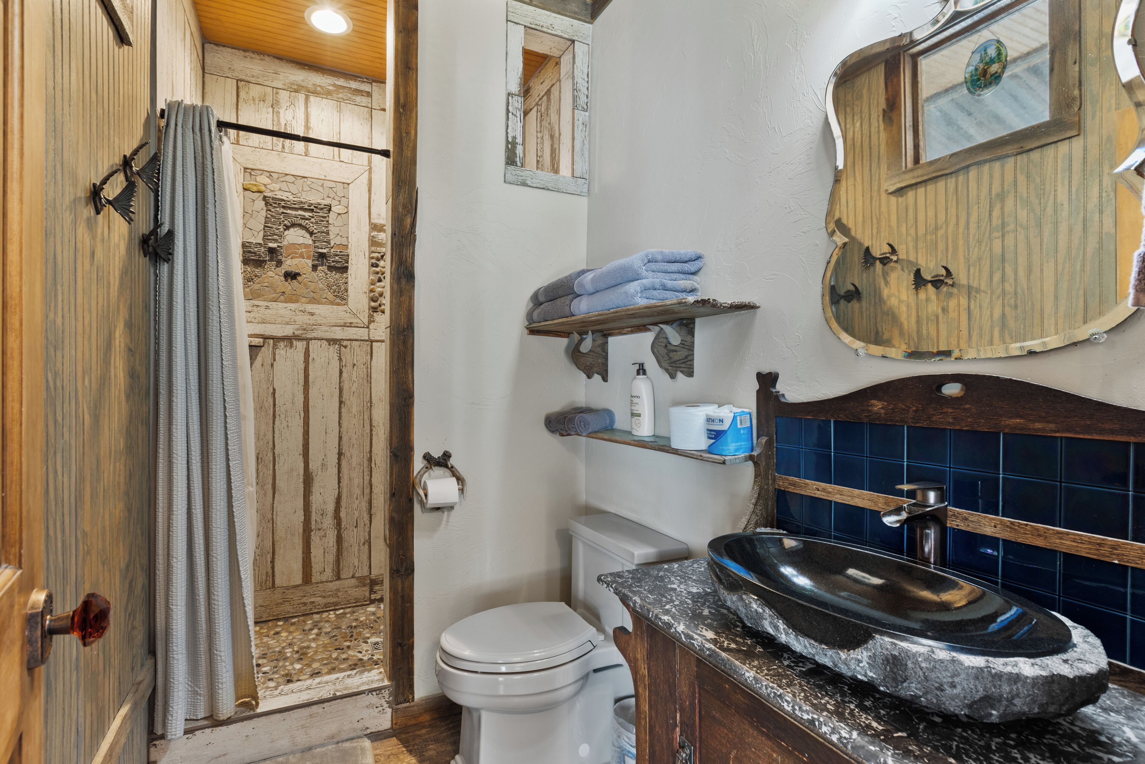 A rustic bathroom with a stone sink, wooden shelves, and a stone fireplace.