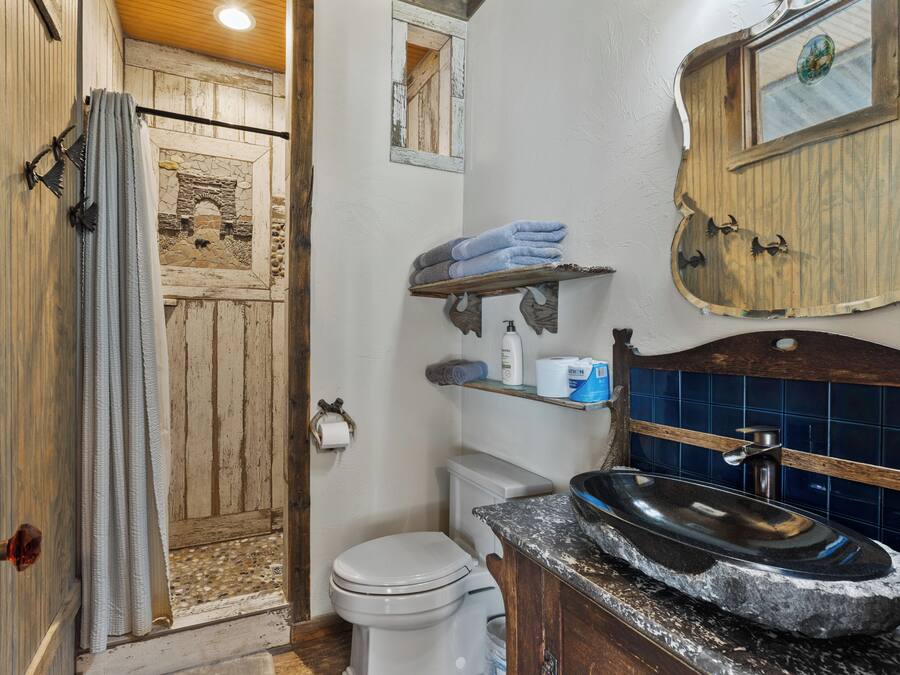 A rustic bathroom with a stone sink, wooden shelves, and a stone fireplace.