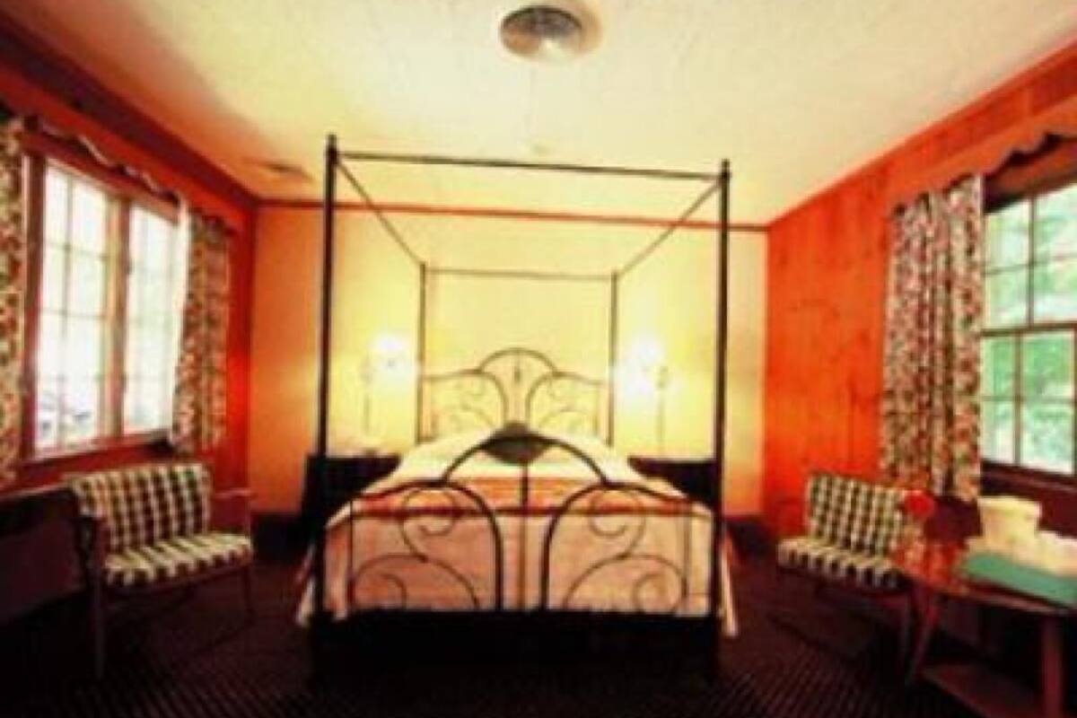 A four-poster bed with a canopy, two bedside tables, and a chair in a room with wooden walls and large windows.