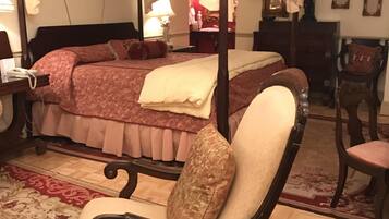 Una cama con dosel y cuatro columnas, con un edredón rojo y beige, una silla de madera con cojín y una alfombra estampada.