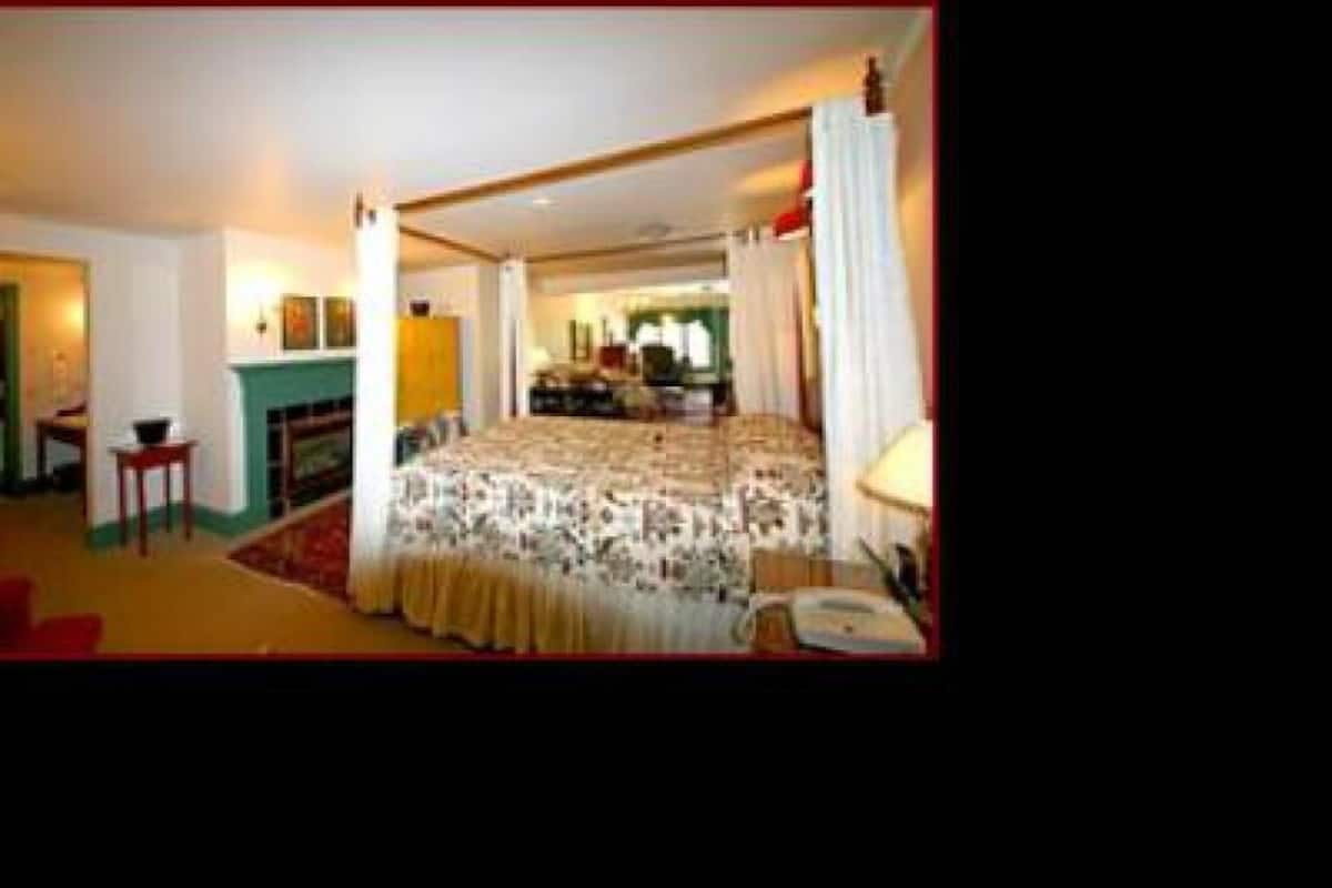 A spacious bedroom with a large bed, a sitting area with a chair and table, and a fireplace.