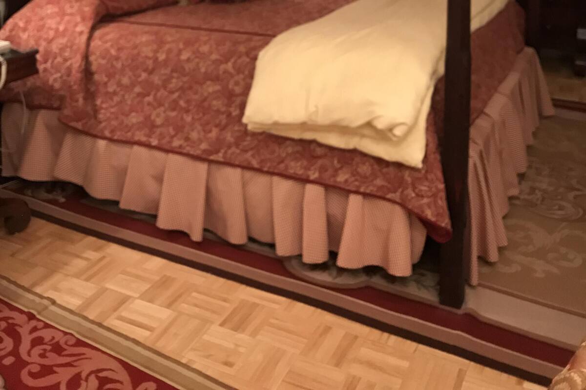 A four-poster canopy bed with a red and white patterned bedspread, a white throw blanket, and a wooden headboard.