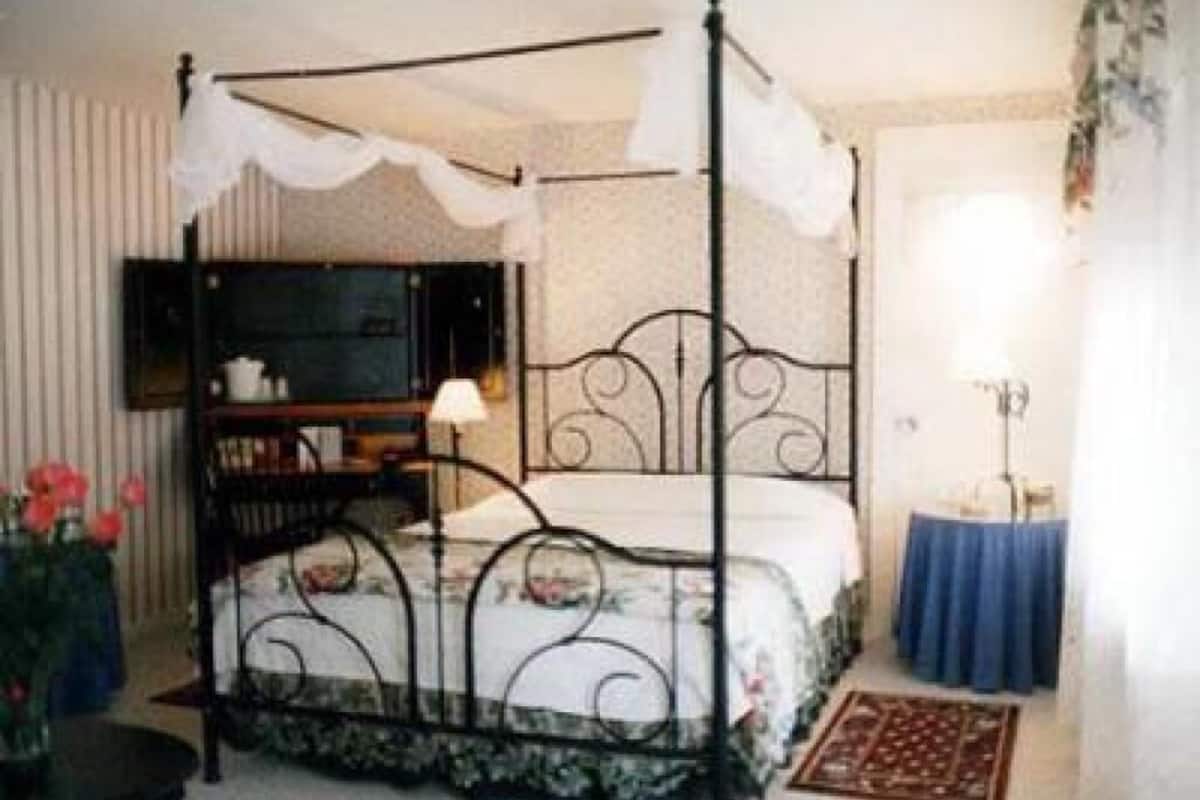 A four-poster bed with a canopy, a bedside table with a lamp, and a small table with a vase of flowers.