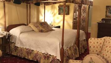 Een bed met hemelbed en bloemenstoffering, een houten nachtkastje met een telefoon en een fauteuil met bloemenprint.